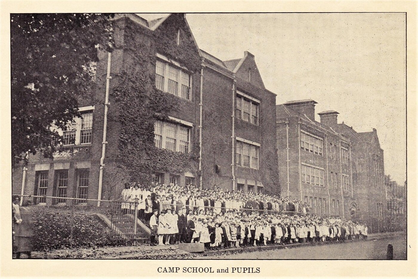 Camp School building covered in ivy with a large group of pupils lined up outside, early 20th century